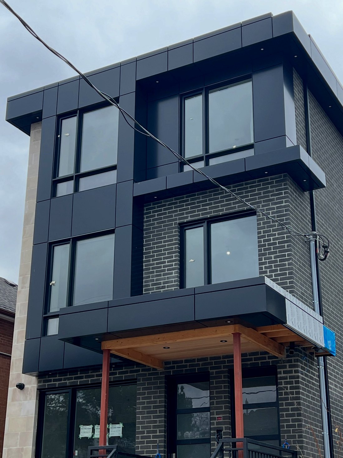 Dark ACM panel facade with grey brick and a wood soffit over the entry, Downtown Toronto