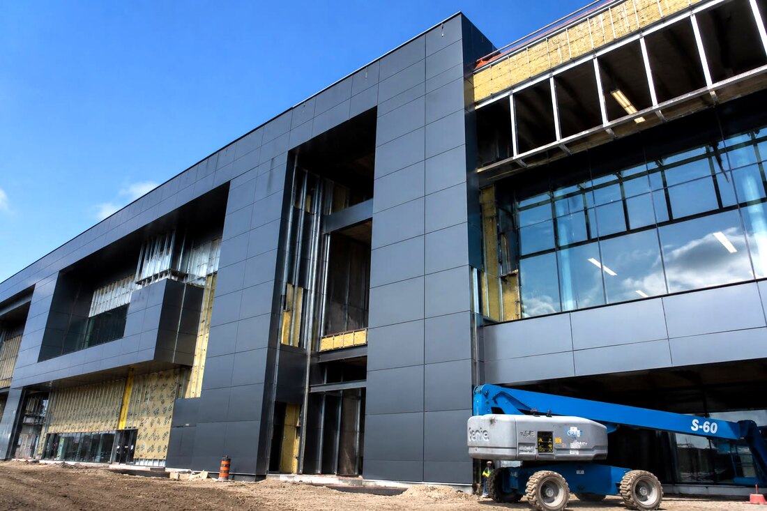 Crew installing dark ACM panels on a commercial building with a boom lift on site