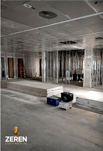 Open floor with ceiling grid in and drywall stacked ready to hang